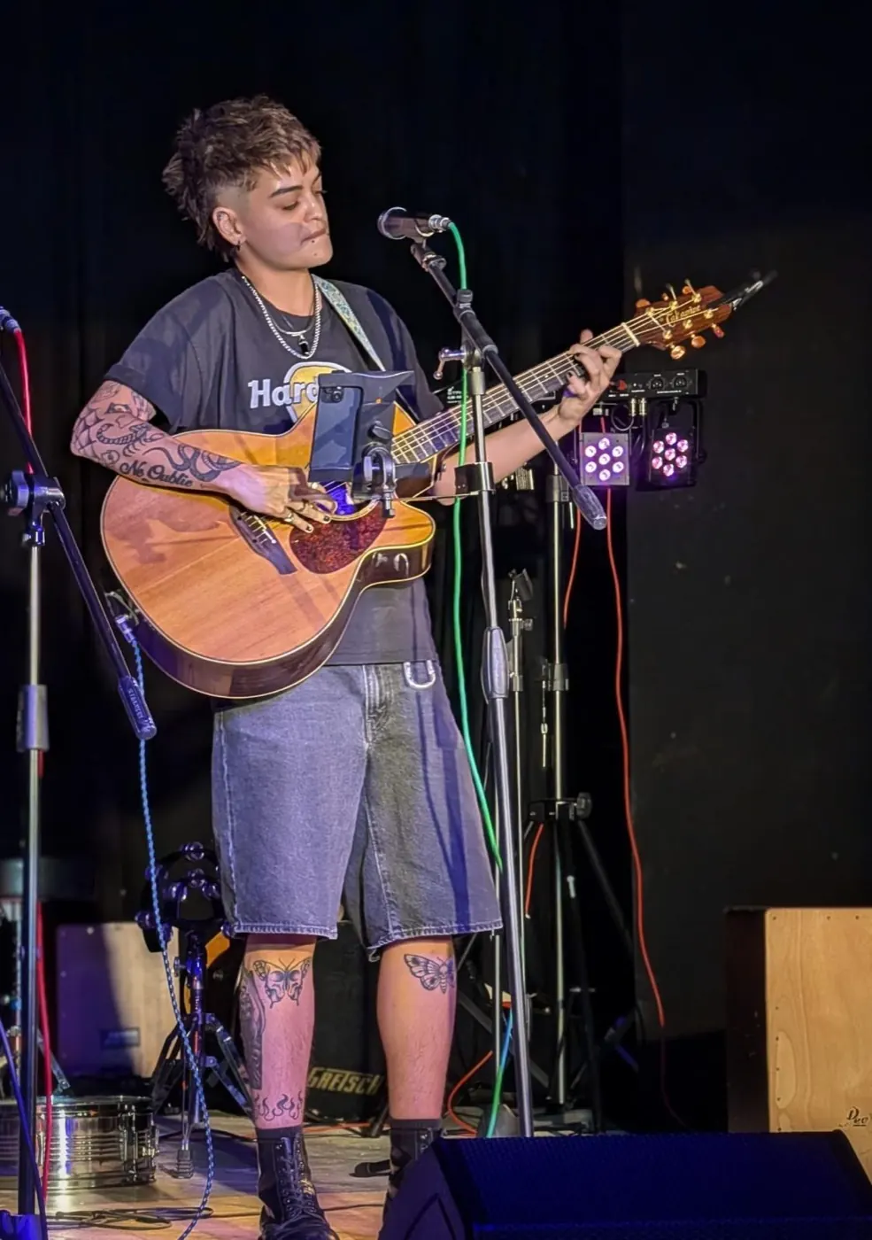 A performer playing acoustic guitar into a microphone at one of the open mic nights