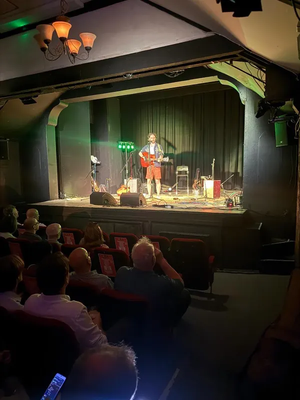 A full audience watching a solo performer on stage at Bromley Little Theatre