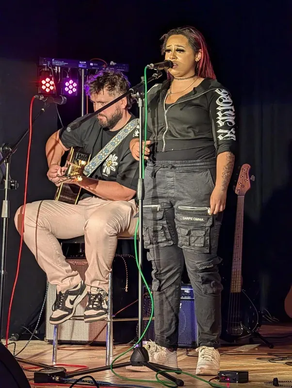A vocalist and seated guitarist performing together at Bromley Little Theatre