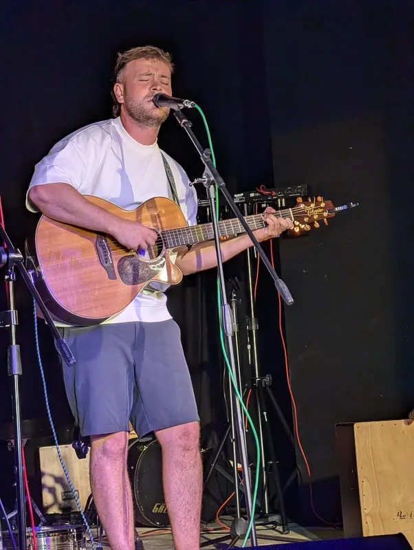 A solo guitarist singing into the microphone at Bromley Little Theatre