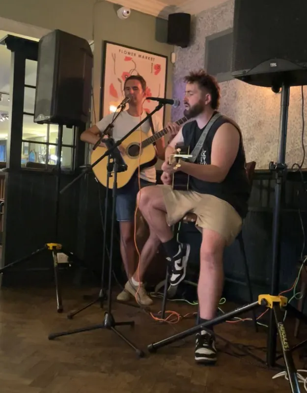 Two performers sharing microphones with acoustic guitars at The Oak
