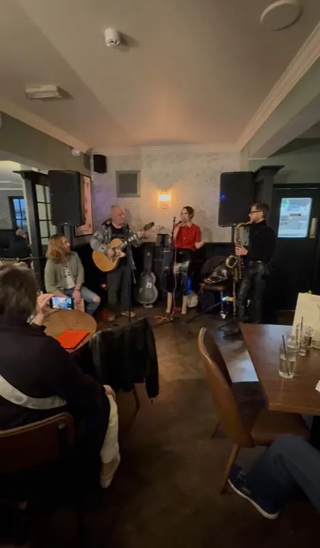 A four-piece playing to a seated crowd at The Oak — acoustic guitar, singer and saxophone