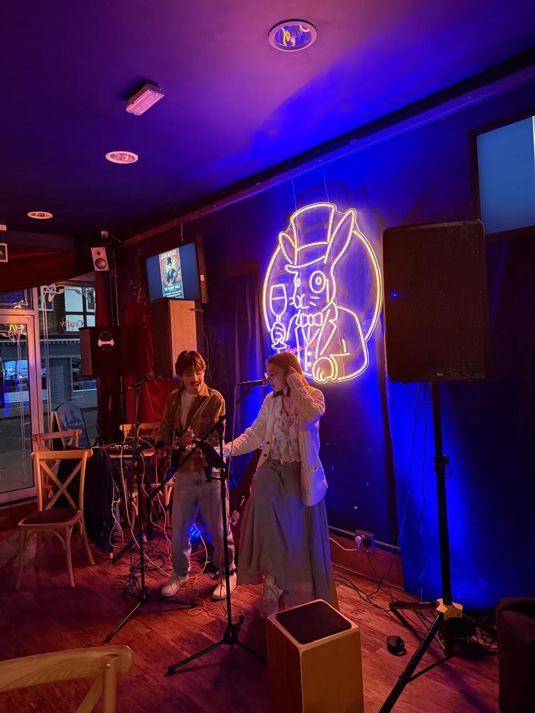 Two singers performing beneath the neon rabbit sign at The Rabbit Hole